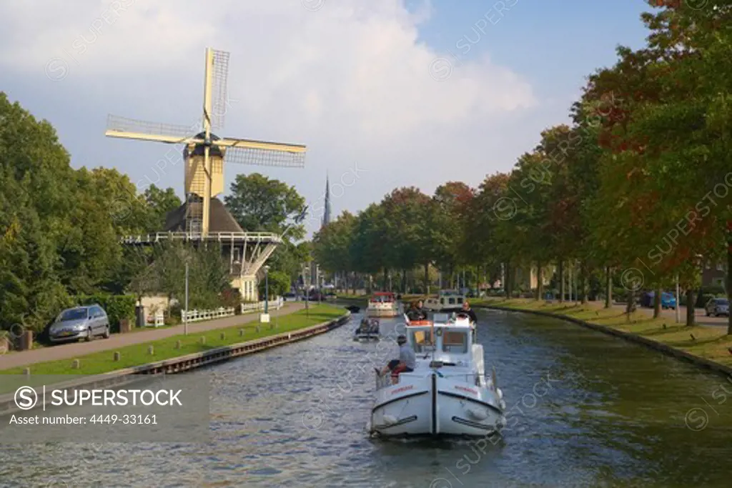 A houseboat on the river Smal Weesp driving past a windmill, Weesp, Netherlands, Europe