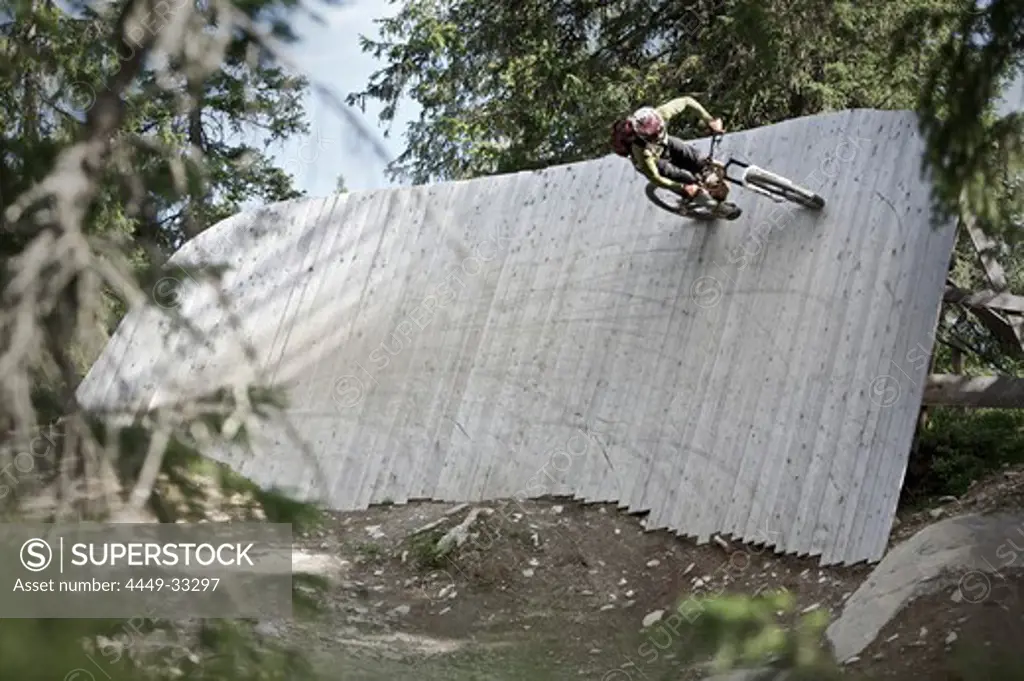Mountainbiker riding on a vertical timber wall, Lillehammer, Norway