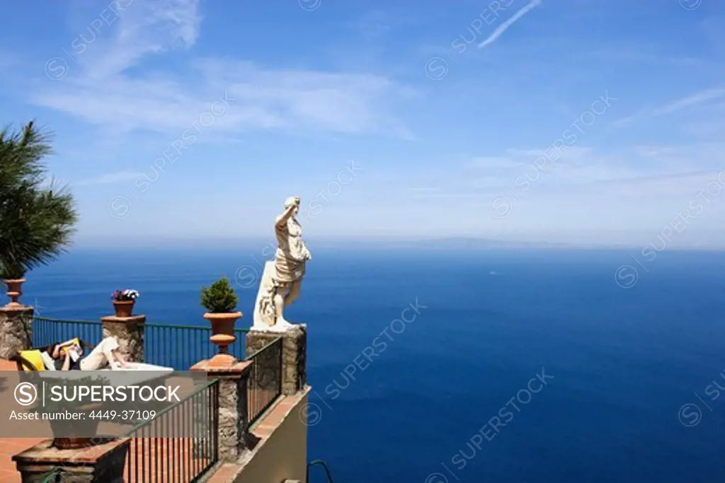 A woman lying reading at a terrace with sea view, Capri, Italy, Europe