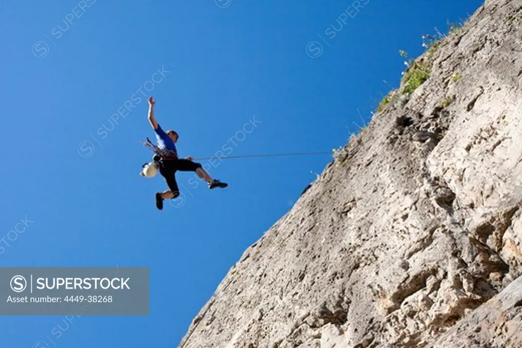 Rock climber abseiling from a rock face under blue sky, Jerzu, Sardinia, Italy, Europe