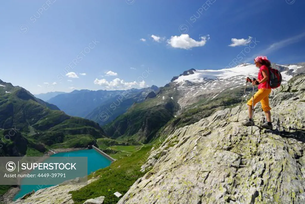 Female hiker looking over reservoir Lago di Robiei, Basodino glacier in background, Ticino Alps, Ticino, Switzerland