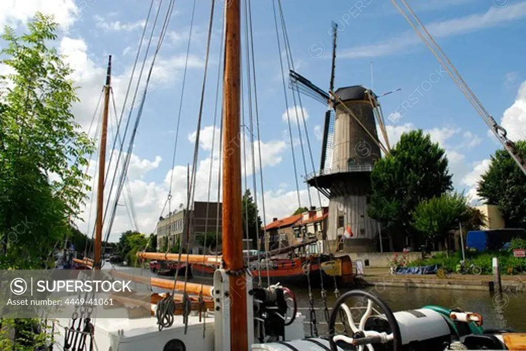 Ships in river port, windmill in background, Gouda, South Holland, The Netherlands