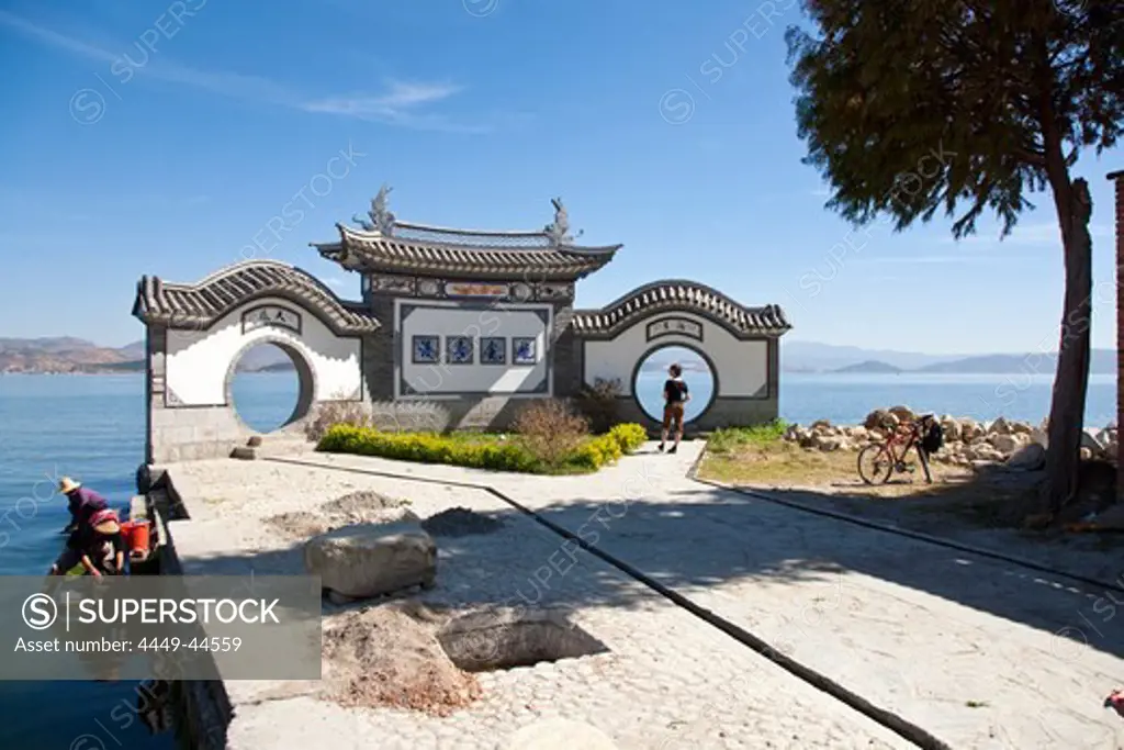 Moon gate at Erhai lake, traditional chinese architecture, tourist with bicycle, women doing the washing, Yunnan, People's Republic of China, Asia