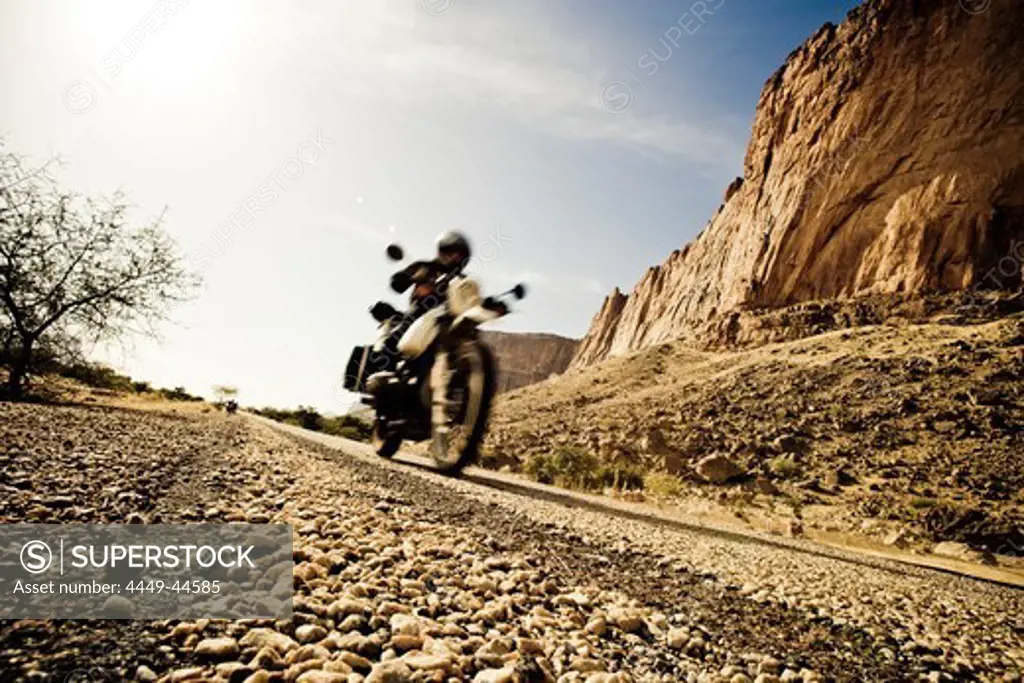 Man on motorcycle on rough-textured tarred road, Mali, Africa