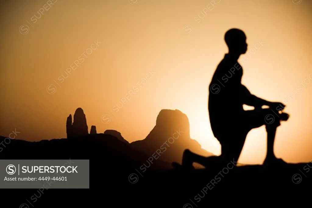 Kneeling boy in front of rock formation at sunset, Hombori, Mali, Africa