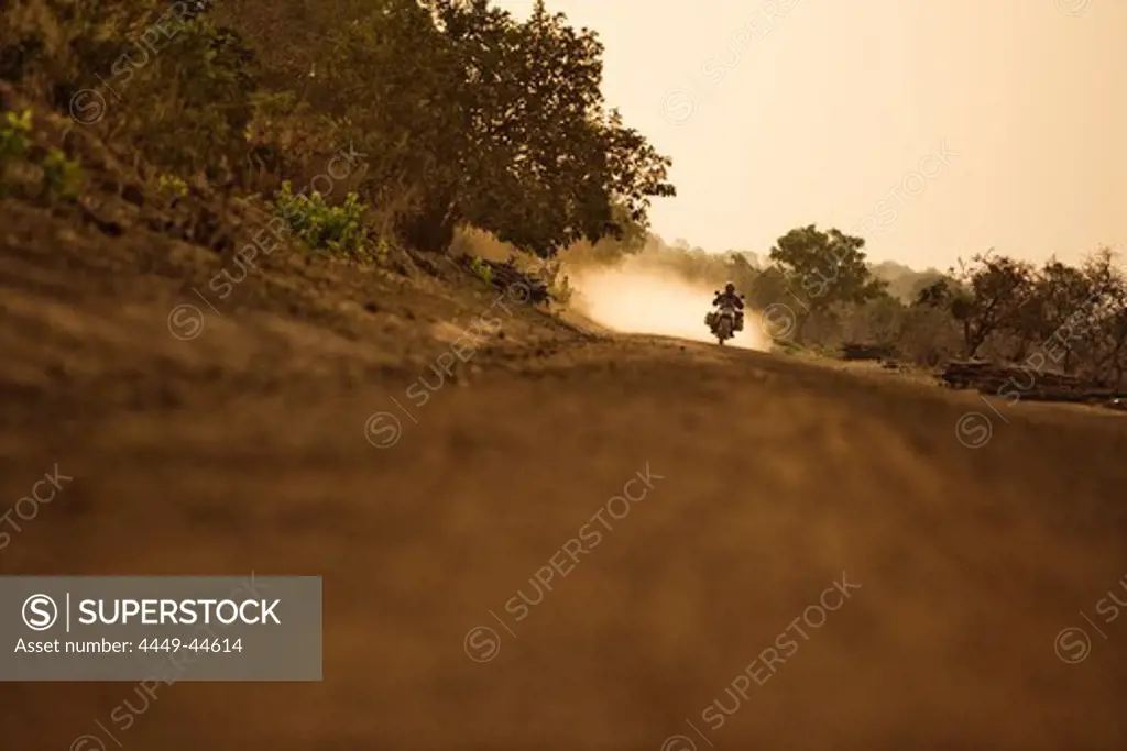 Man on motorcycle riding on a dirt road in the evening, Mali, Africa