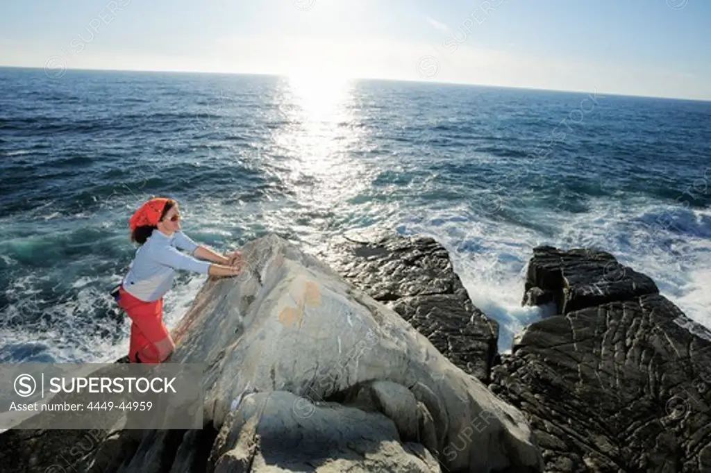 Woman climbing a rock on the Mediterranean coast, Liguria, Italy