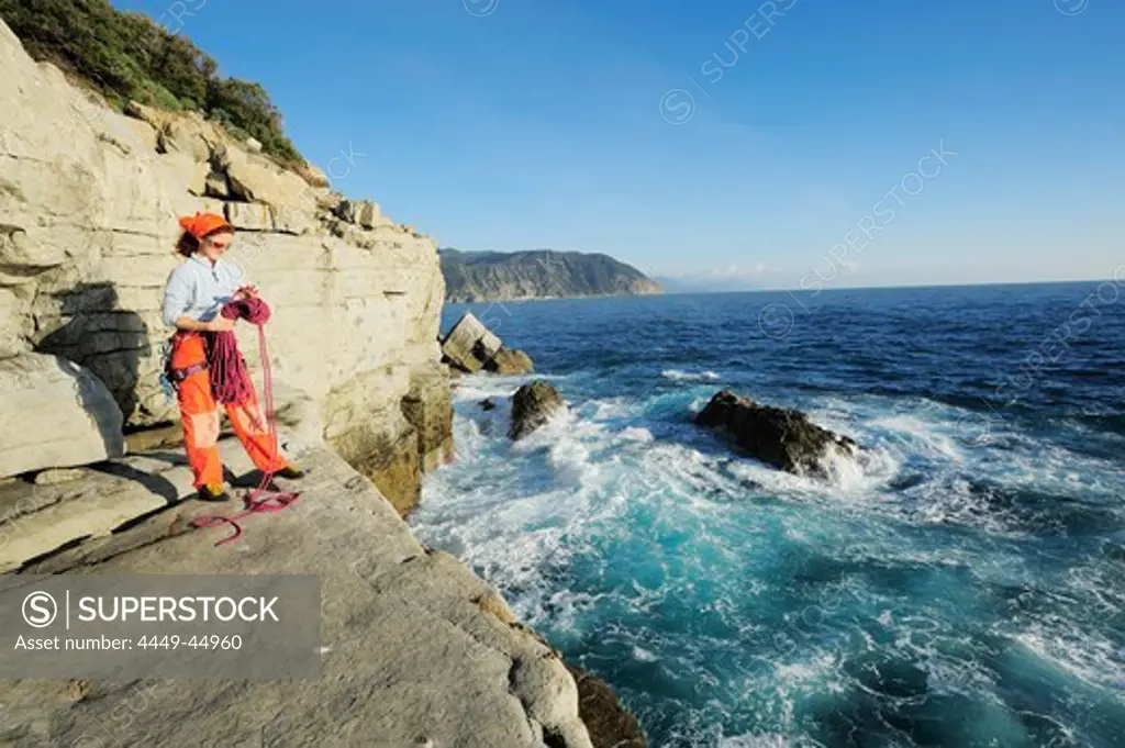Woman holding a climbing rope and preparing for climbing, cliff at the Mediterranean coast, Liguria, Italy