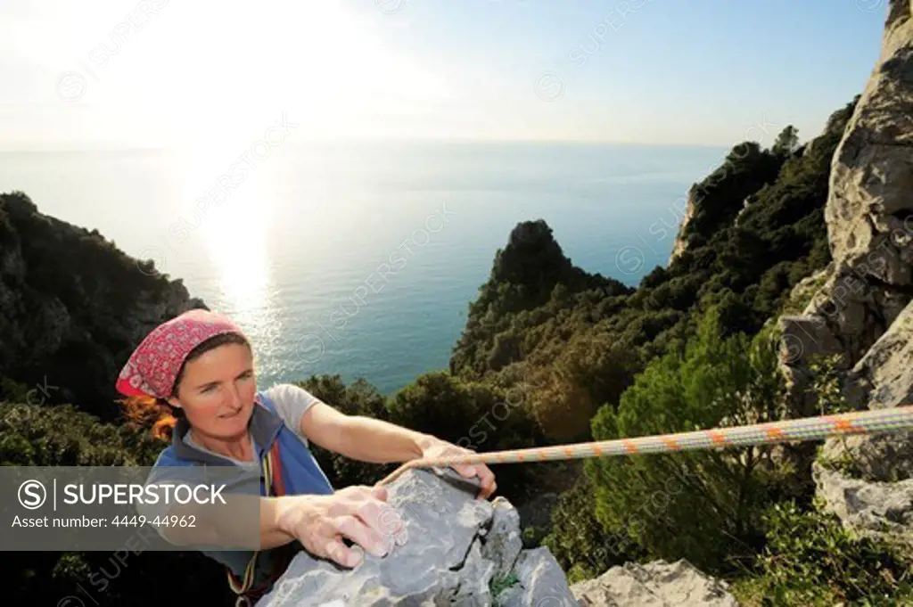 Woman climbing a rock face high above the Mediterranean sea, natural park Porto Venere, national park Cinque Terre, UNESCO world heritage site, Liguria, Italy