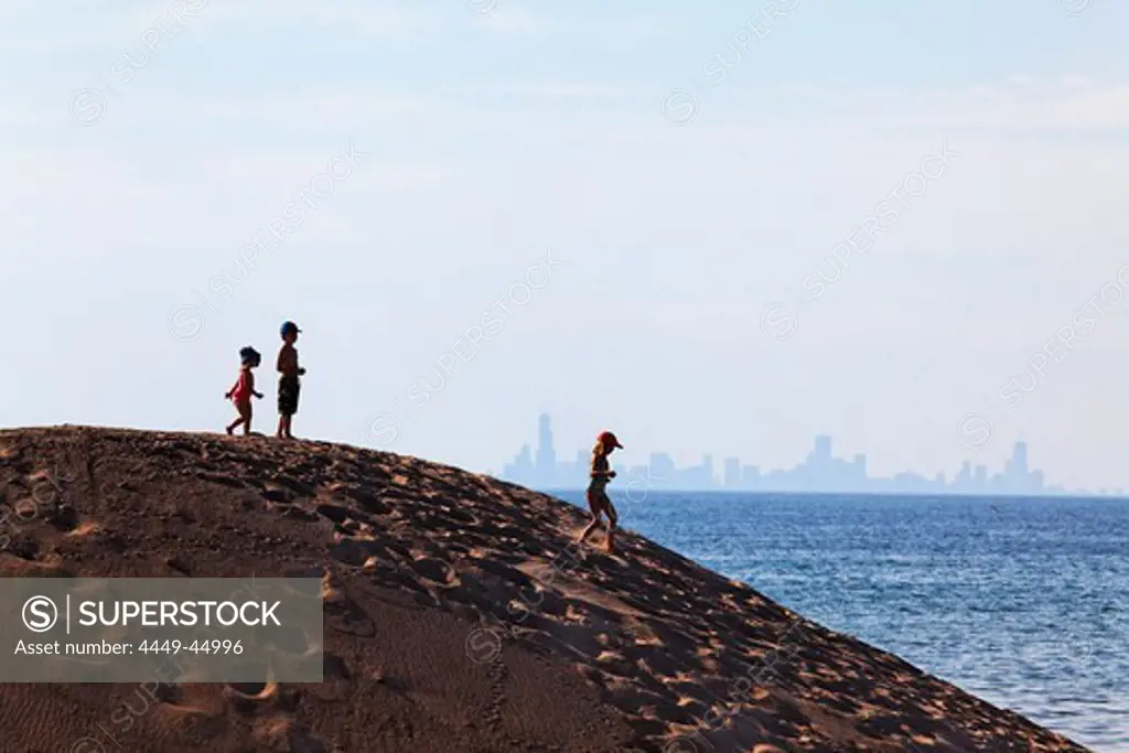 Kids standing on a sand dune in Indiana Dunes National Lakeshore park, silhouette of Downtown Chicago in the background, Indiana, USA