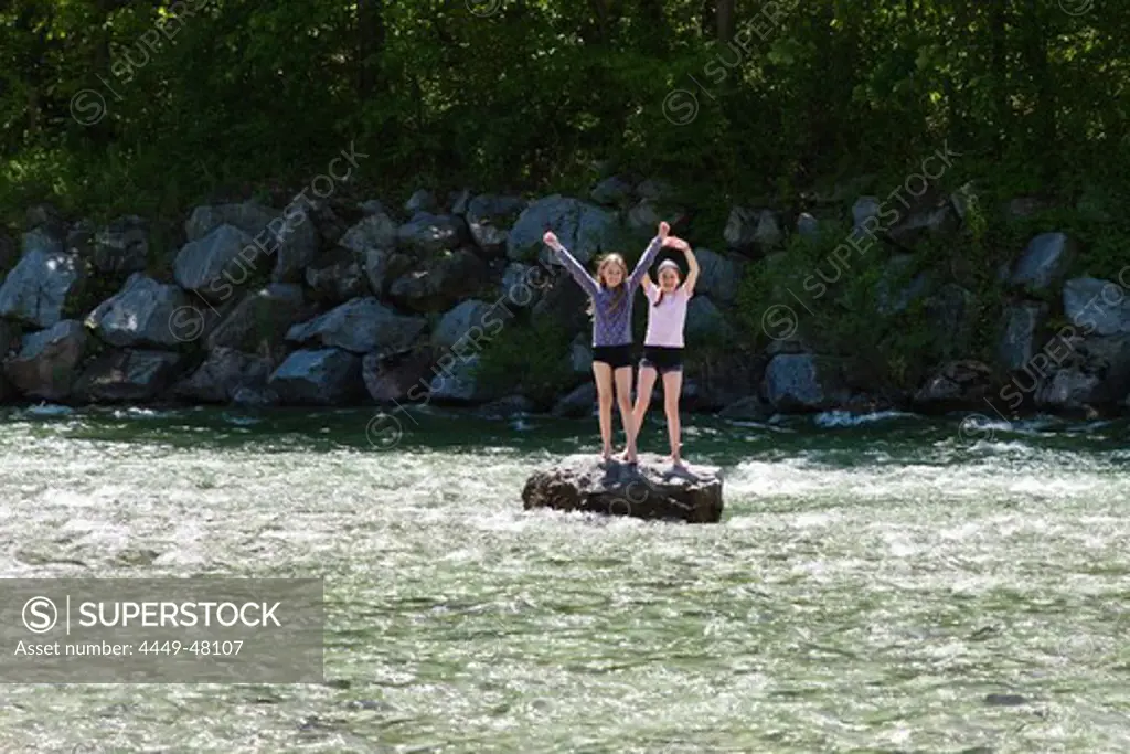 Two girls (10 years) standing on rock in river Isar, near Fleck, Isar Cycle Route, Upper Bavaria, Germany