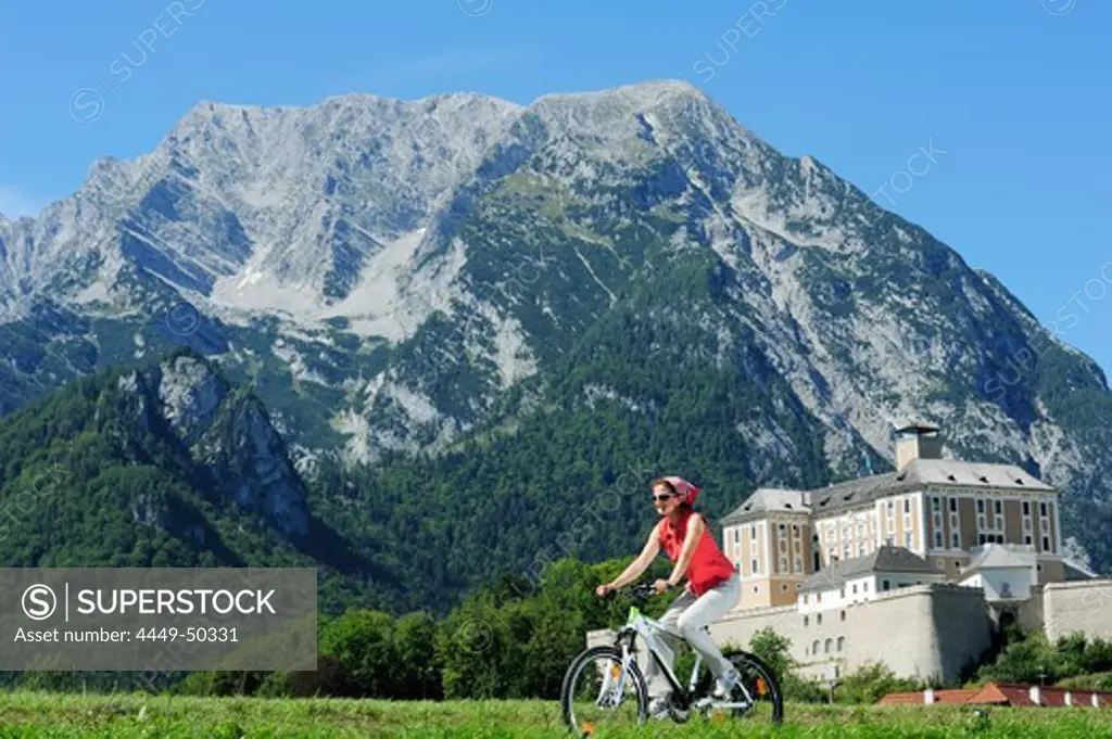 Woman riding a bike on Ennstal bicycle route with palace Trautenfels and Grimming in background, valley of Ennstal, Ennstal bicycle route, Styria, Austria