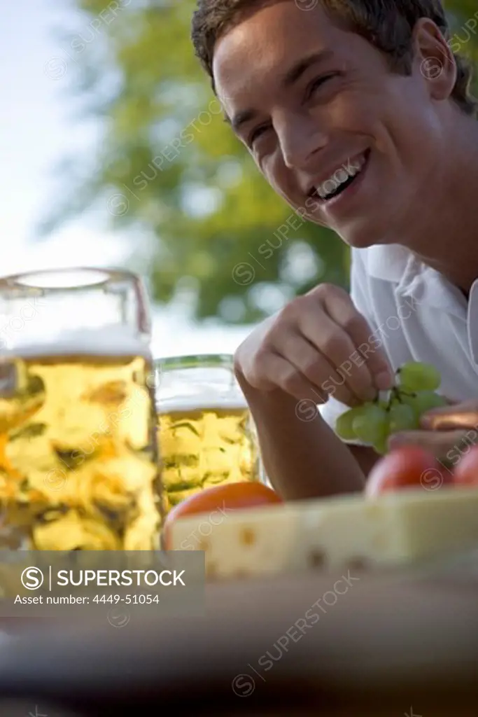 Young man with snack and beer stein in beergarden near Lake Starnberg, Bavaria, Germany