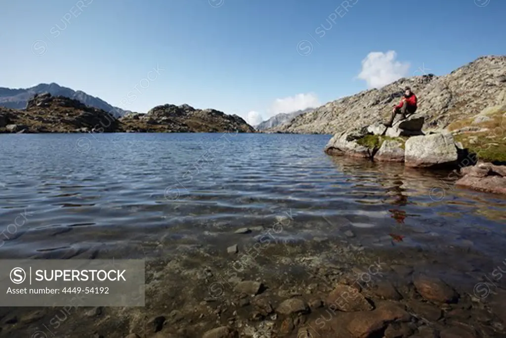 Hiker resting at mountain lake Estany de Monges, Carros de Foc, Aiguestortes i Estany de Sant Maurici National Park, Catalonia, Spain