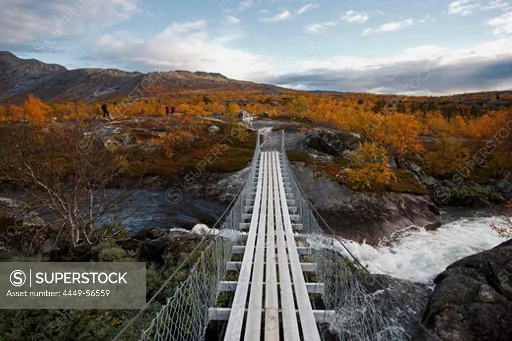 Wooden swing bridge across a river in a rocky landscape with birch trees north of the arctic circle, Saltdal, Junkerdalen national park, trekking tour in Autumn, Fjell, Lonsdal, near to Mo i Rana, Nordland, Norway, Scandinavia, Europe
