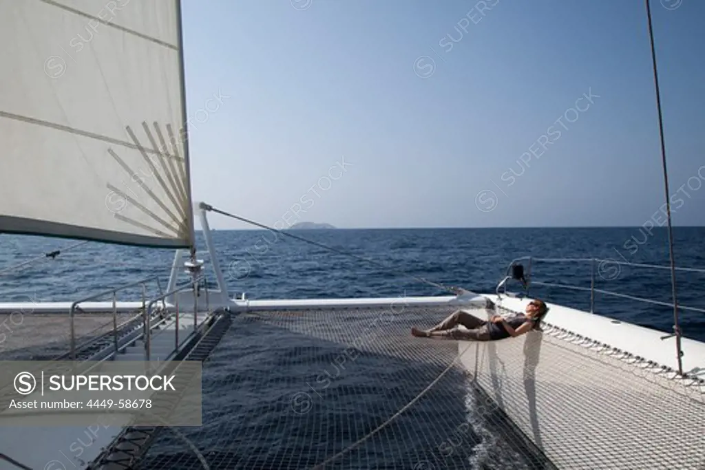 Woman relaxes on net of catamaran SY Azzura, Ocean Blue Oman cruises, during sailing excursion, Muscat, Masqat, Oman, Arabian Peninsula