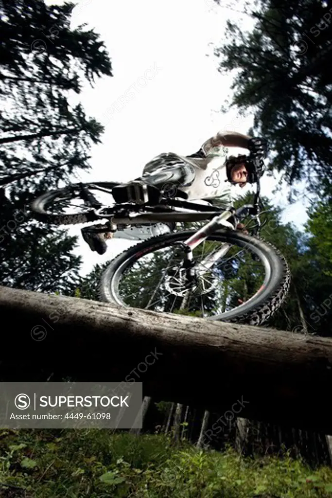 Young man riding a mountainbike on a trunk, Oberammergau, Bavaria, Germany