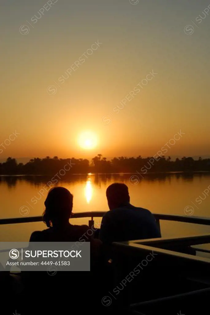cruise on the Nile, couple on upper deck, sunset above palm trees at western bank, Nile between Luxor and Dendera, Egypt, Africa