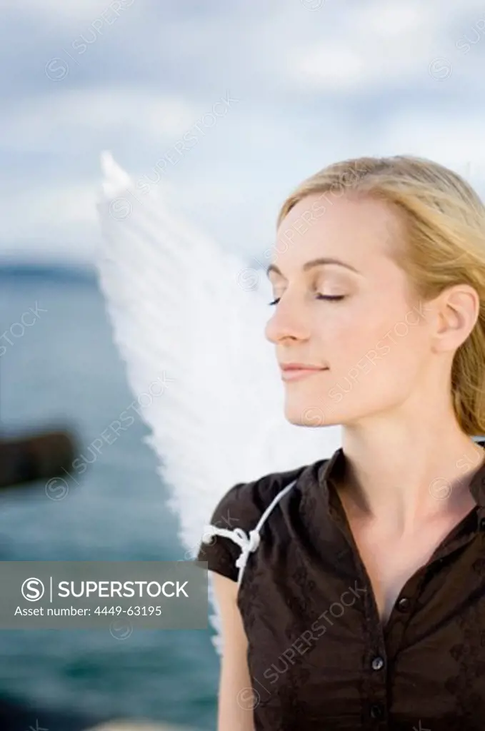 Mid adult woman wearing angel wings smiling