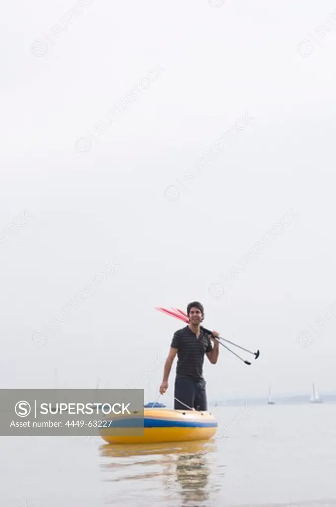 Young man pulling rubber dingy to shore, Lake Ammersee, Bavaria, Germany