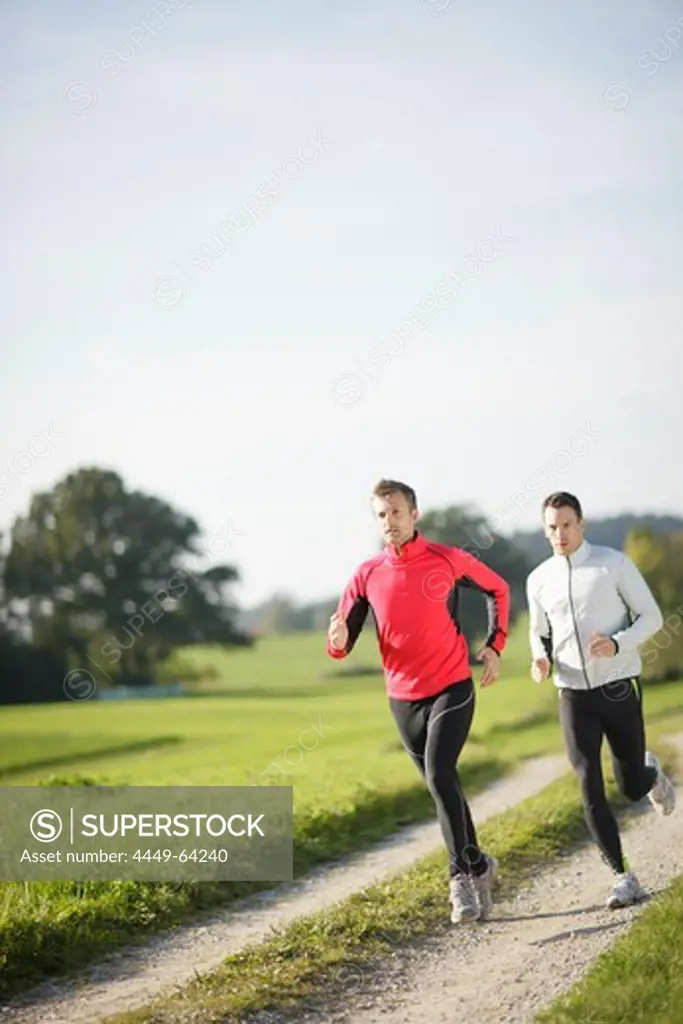 Two men running along dirt road, Munsing, Bavaria, Germany