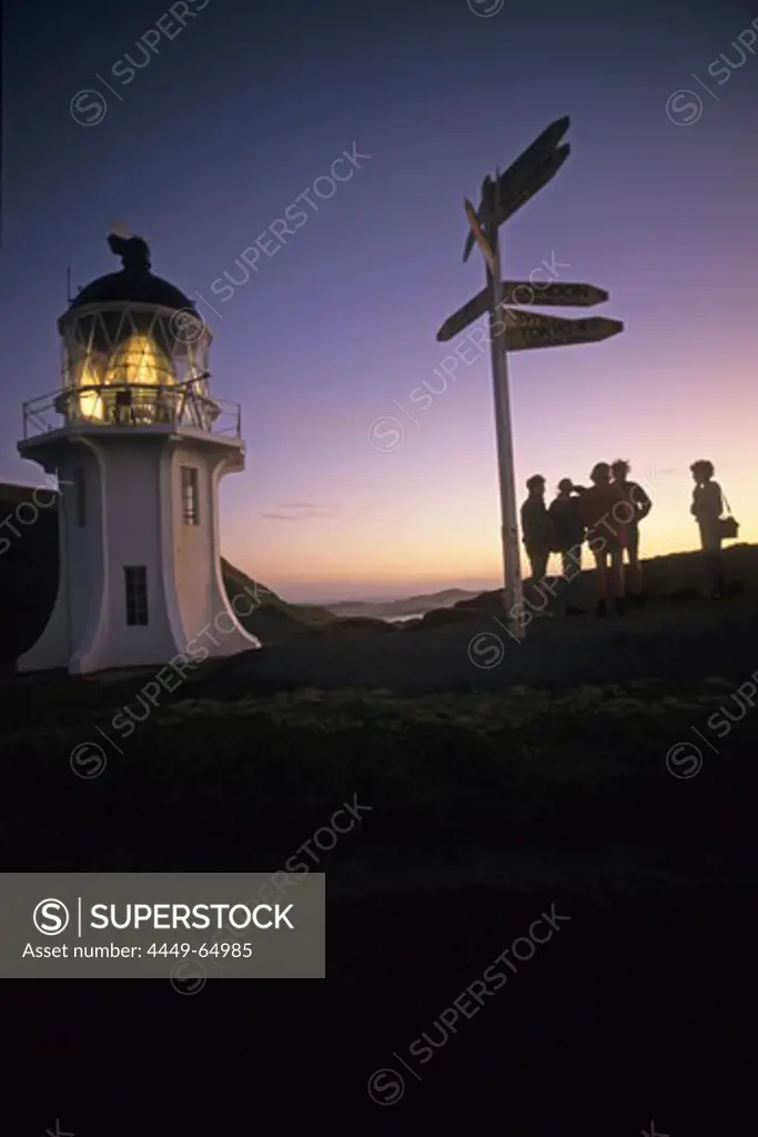People in the sunset with lighthouse and signpost, Cape Reinga, northernmost point of New Zealand, North Island, New Zealand