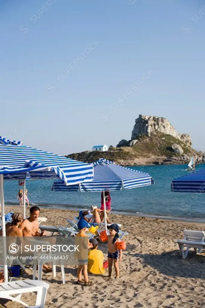 People sunbathing at Kefalos beach, Kastri island with chapel St. Nicholas in background, Kefalos, Kos, Greece