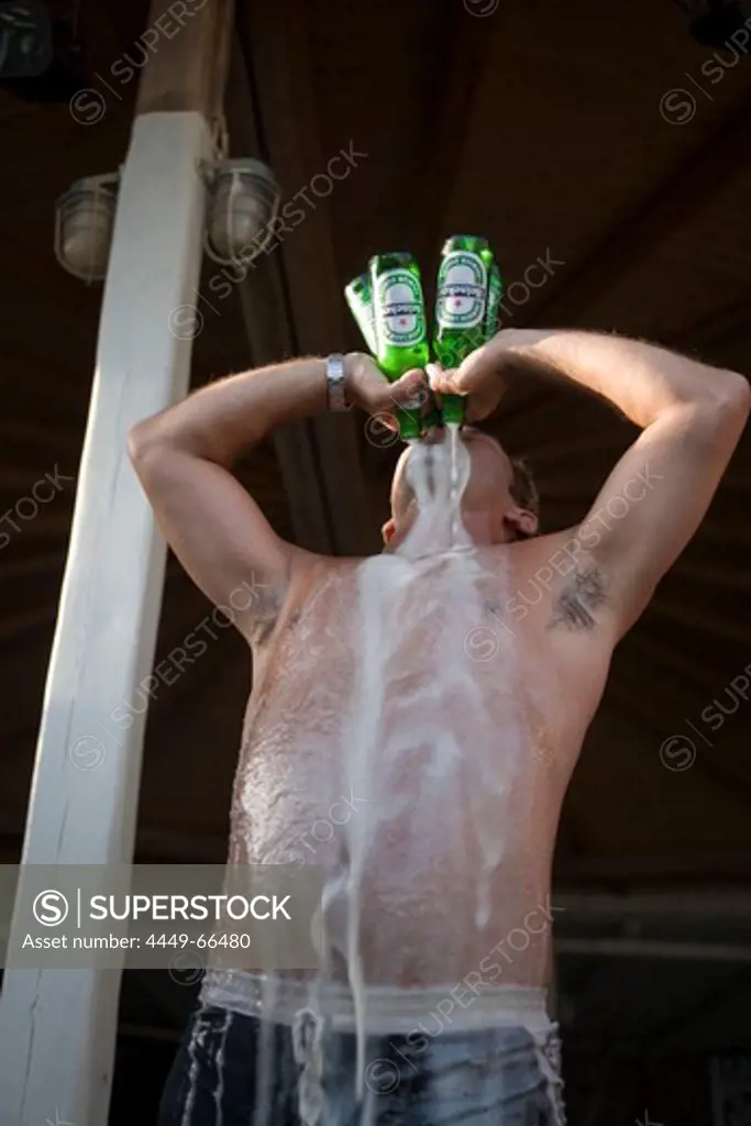 Man drinking four bottles of beer all at once during a beach party of the Super Paradise Club at Super Paradise Beach, knowing as a centrum of gays and nudism, Psarou, Mykonos, Greece