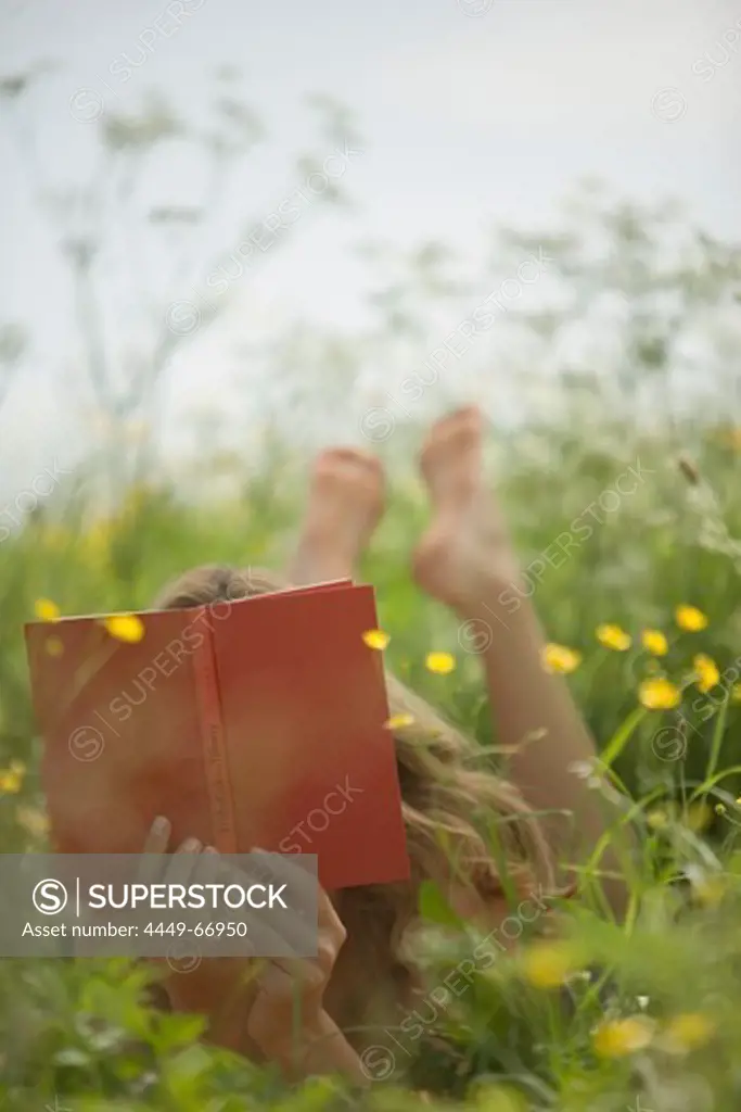 Young woman lying on meadow and reading book