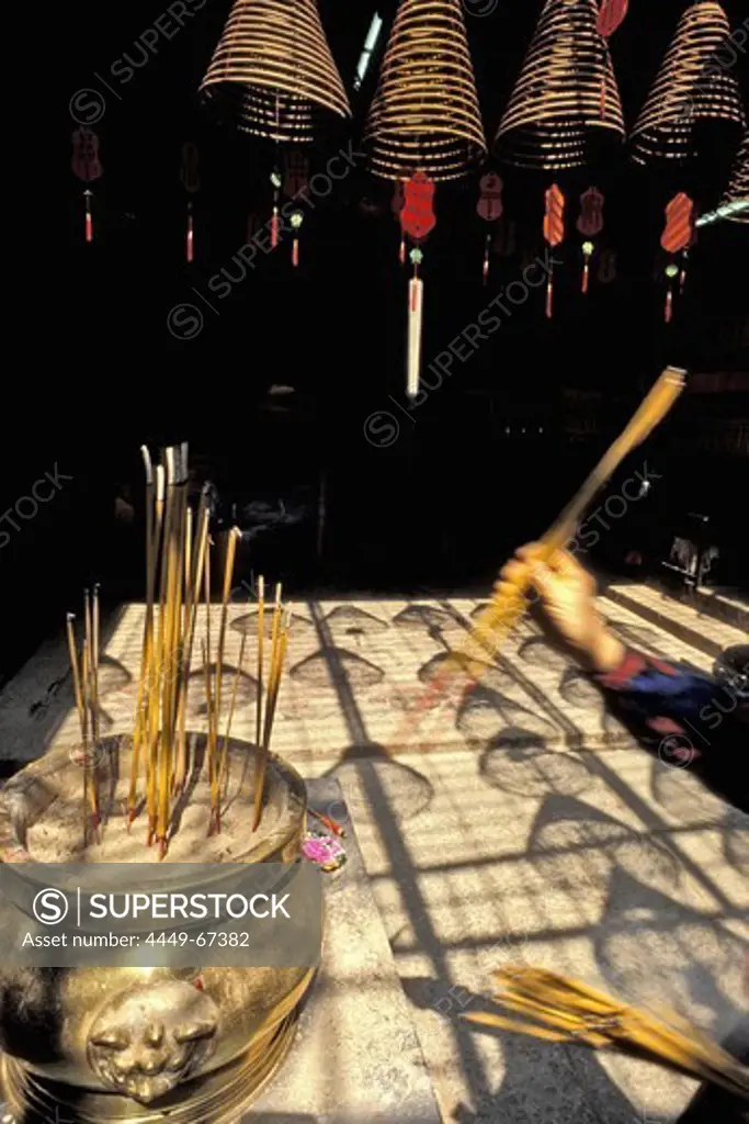 Spiral incense coils hanging from a temple ceiling, Woman lighting an incense stick in the foreground, China