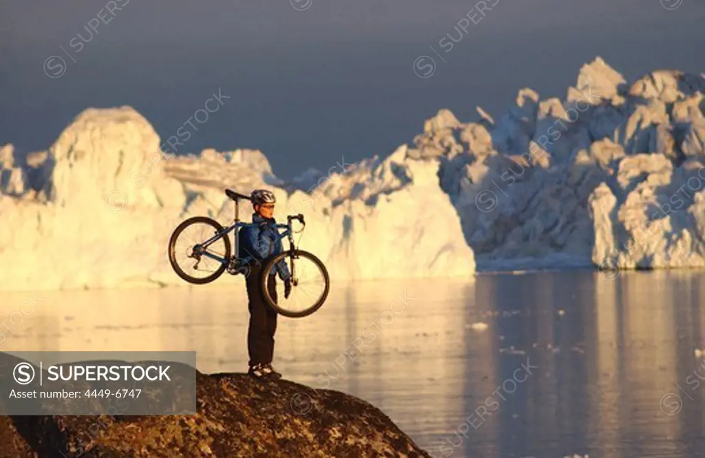 Female mountainbiker carrying her bike, admiring the views, Ilulissat, Greenland