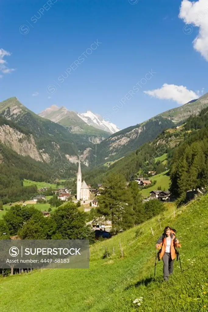Woman hiking over alp above Heiligenblut with pilgrimage church Zum hl. Pluet, view to Grossglockner, Heiligenblut, Carinthia, Austria
