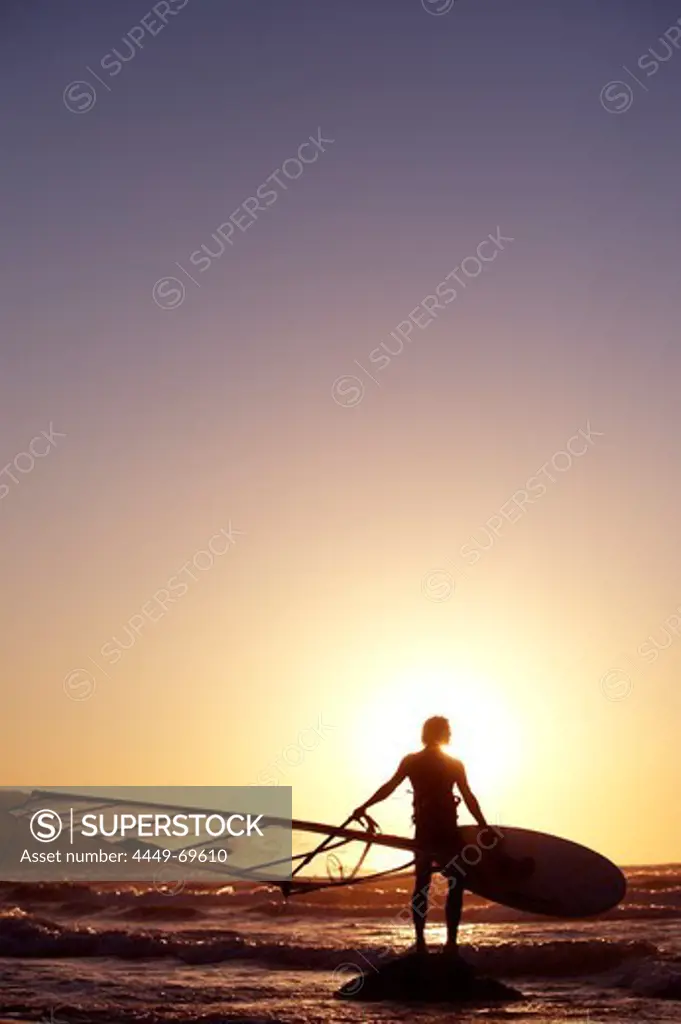 Windsurfer standing on the beach against sunset with his surfboard, Kos, Greece