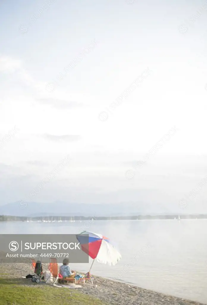 Woman with sunshade on the lake shore, Ambach, Lake Starnberg, Bavaria, Germany