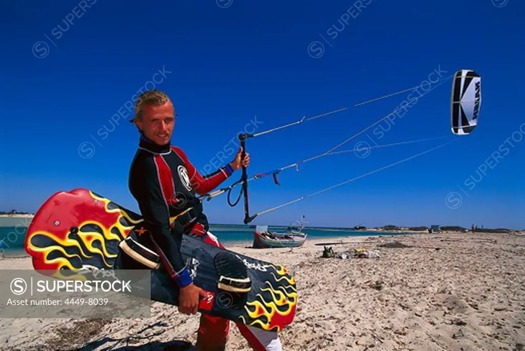 Kitesurfer walking along the beach with his board and kite, Djerba, Tunesia