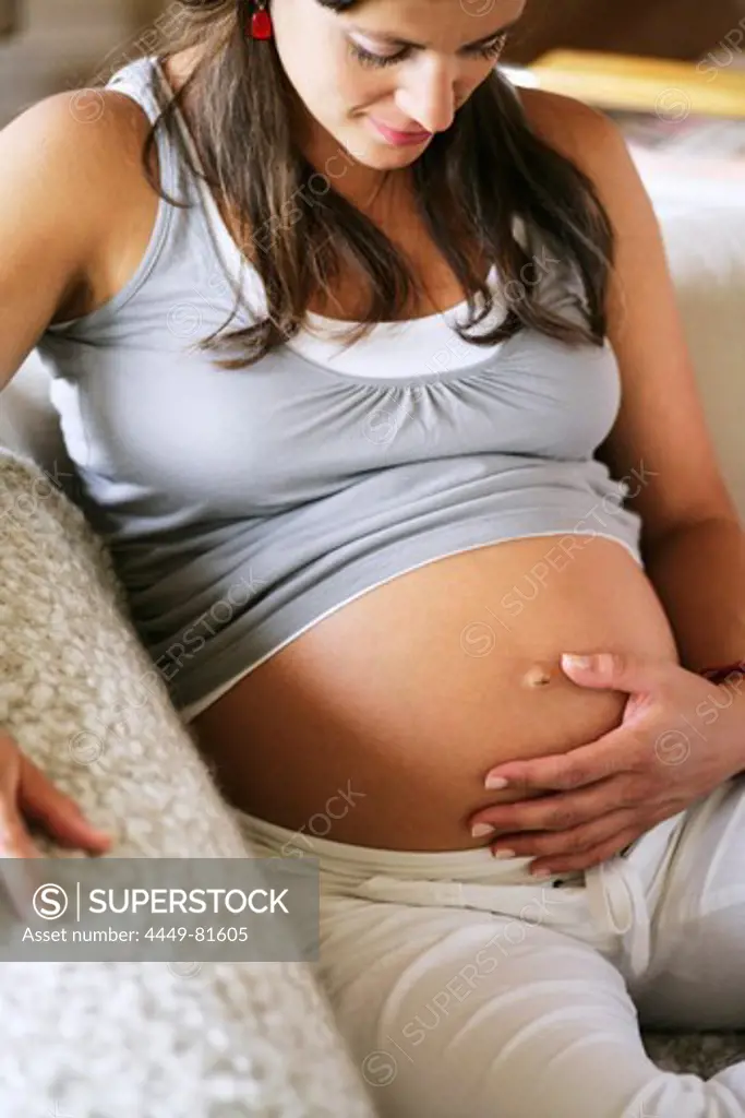 Pregnant woman sitting on a sofa while touching belly, Styria, Austria