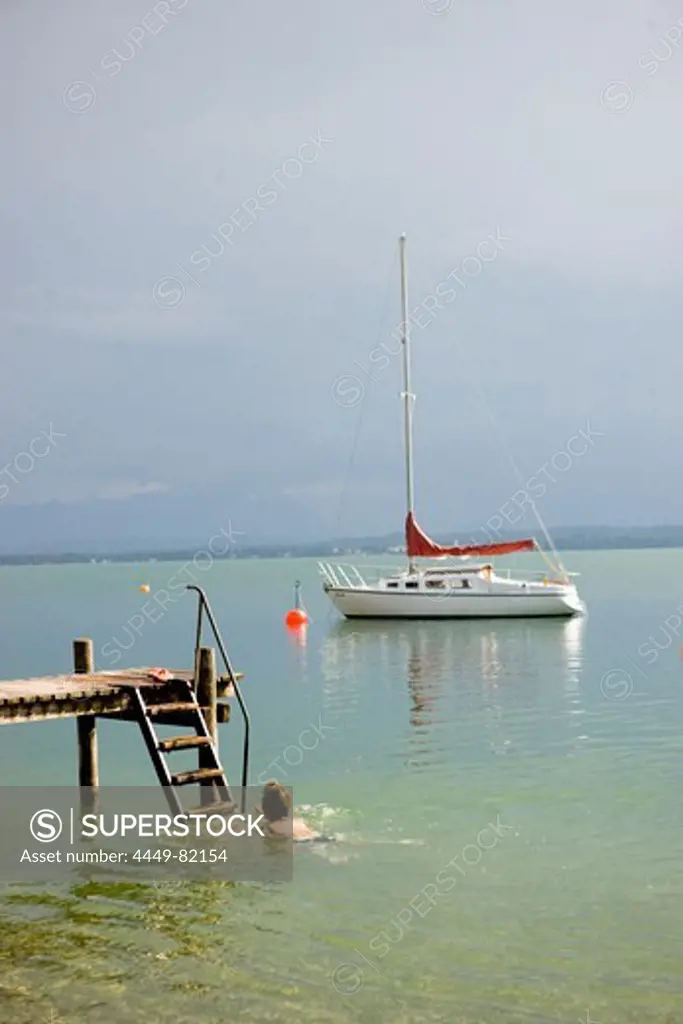 Person near jetty, sailboat in background, Lake Starnberg, Bavaria, Germany