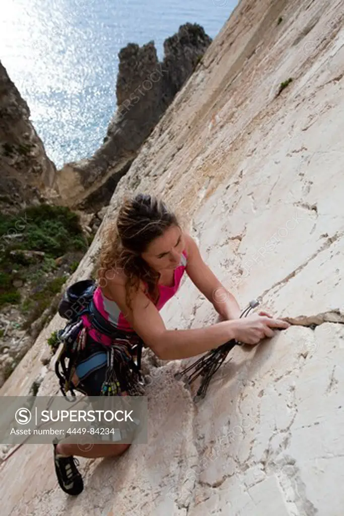 A young woman, a climber, a sportclimber, freeclimber, climbing at Ix-Xaqqa rock face, Malta, She protects with nuts and wires, Europe