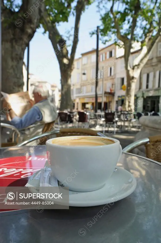 Coffee cup and old man with newspaper at a street cafe under trees, Place des Corps Saints, Avignon, Vaucluse, Provence, France, Europe
