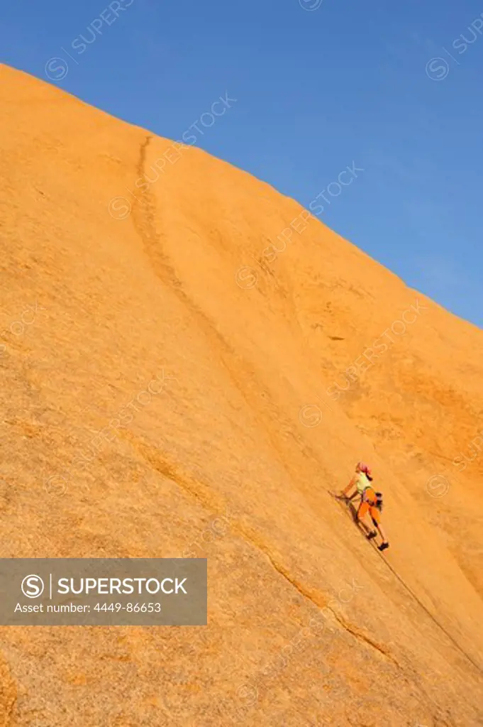 Woman climbing at red rock face, Great Spitzkoppe, Namibia