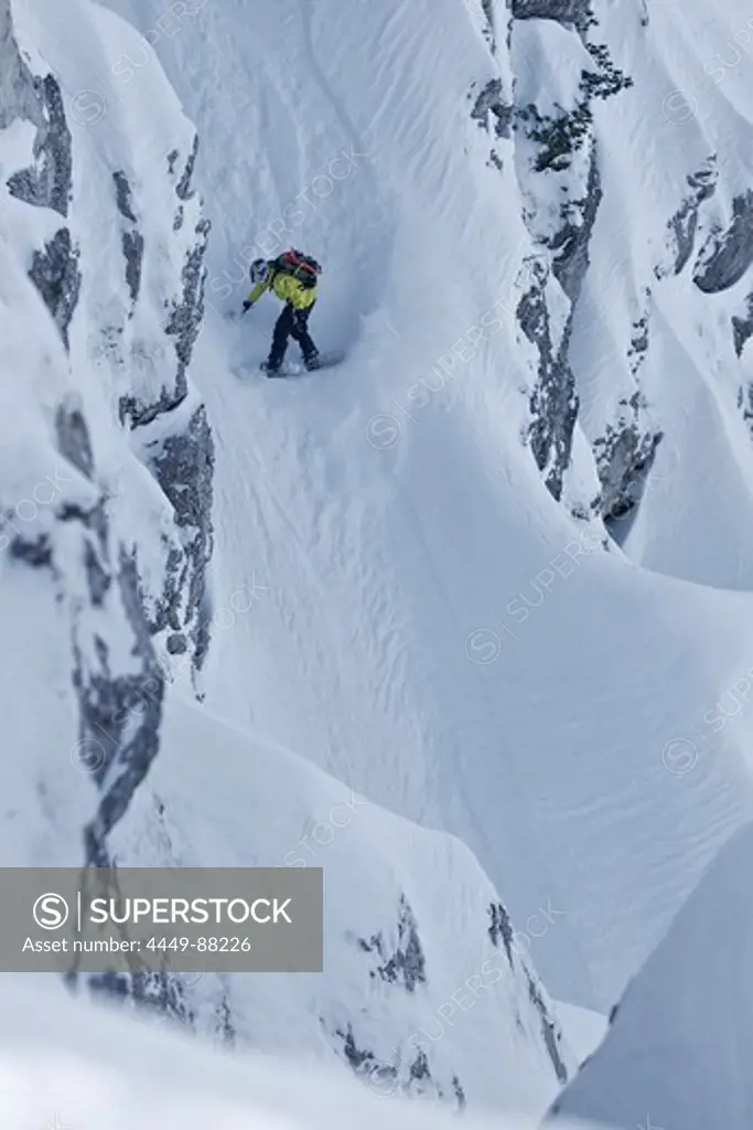 Snowboarder riding in the deep snow between rocks aside the slope, Oberjoch, Bavaria, Germany