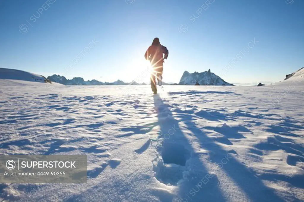 Man running over glacier towards sunrise, overlooking Les Grandes Jorasses and Dent du Geant, Chamonix Mont Blanc, France, Europe