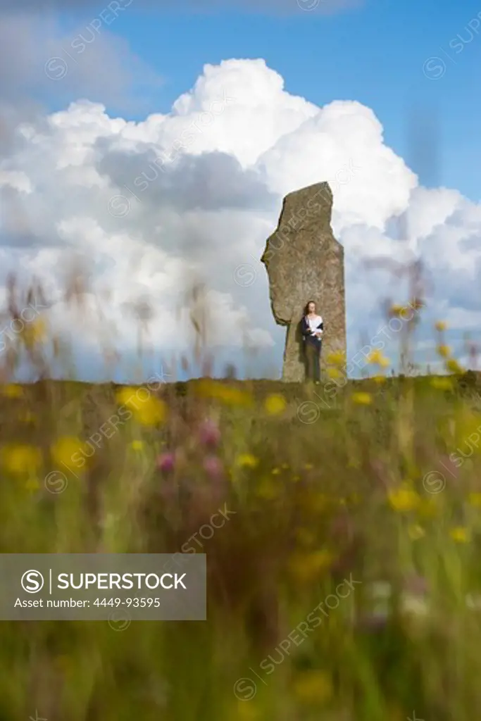 Young woman stands by stone at The Ring of Brodgar circle of Neolithic standing stones, Orkney Islands, Scotland, United Kingdom
