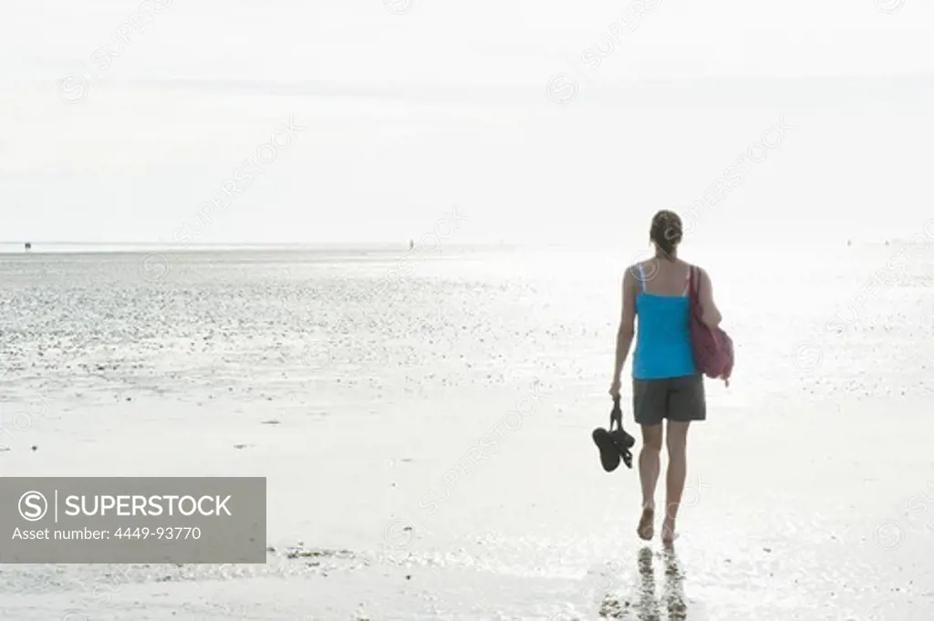 Woman walking barefooted through intertidal mudflats, Wattenmeer National Park, near Wyk, Foehr, North Frisian Islands, Schleswig-Holstein, Germany, Europe