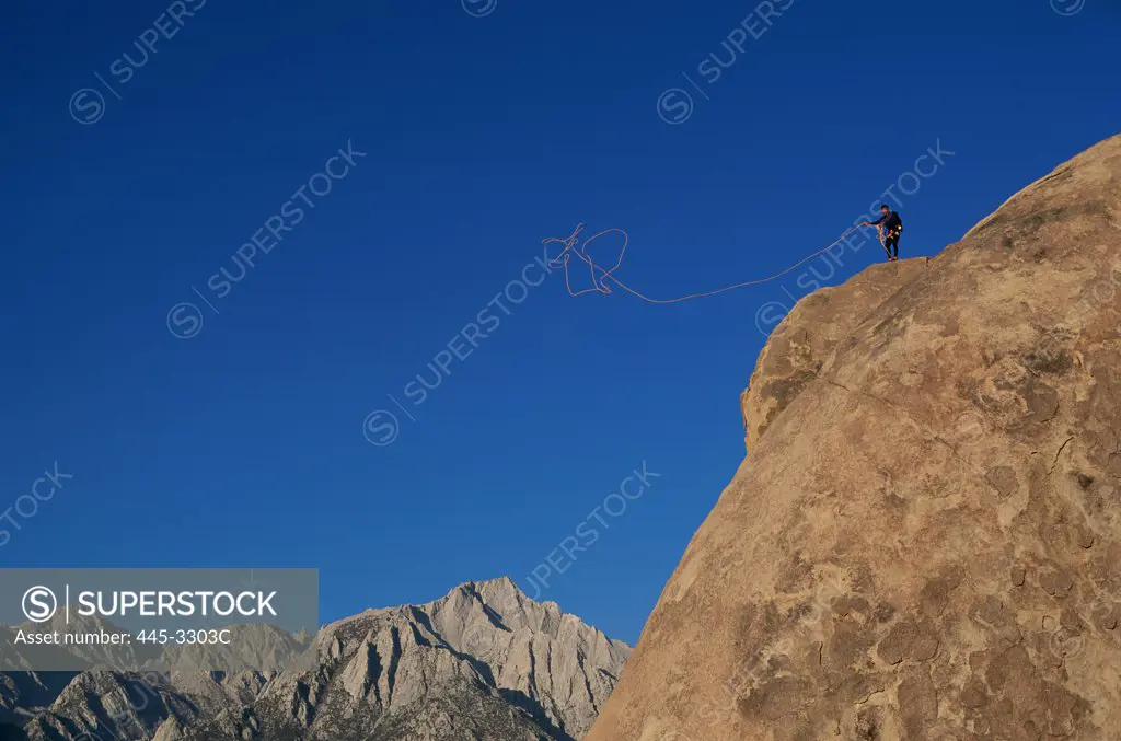 Man standing on the edge of a cliff throwing a rope over, Alabama Hills, South Sierras, California, USA