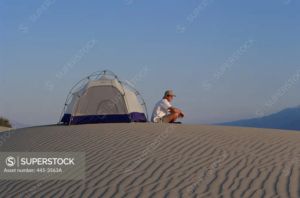 Man sitting outside a tent on a sand dune in Death Valley National Monument, California, USA