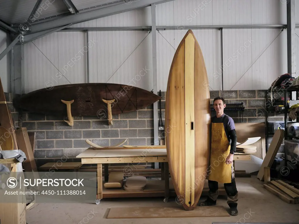 Portrait of man holding hand made wooden paddleboard in workshop