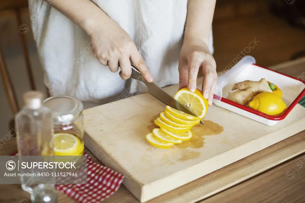 High angle close up of person cutting lemon with knife on wooden cutting board.