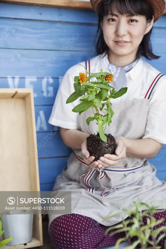 Japanese woman sitting outside a farm shop, planting flowers into flower pots.