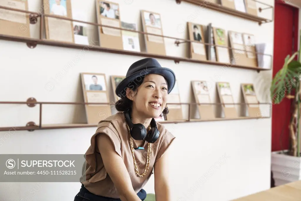 Female Japanese professional wearing Trilby hat and headphones sitting  in a co-working space.